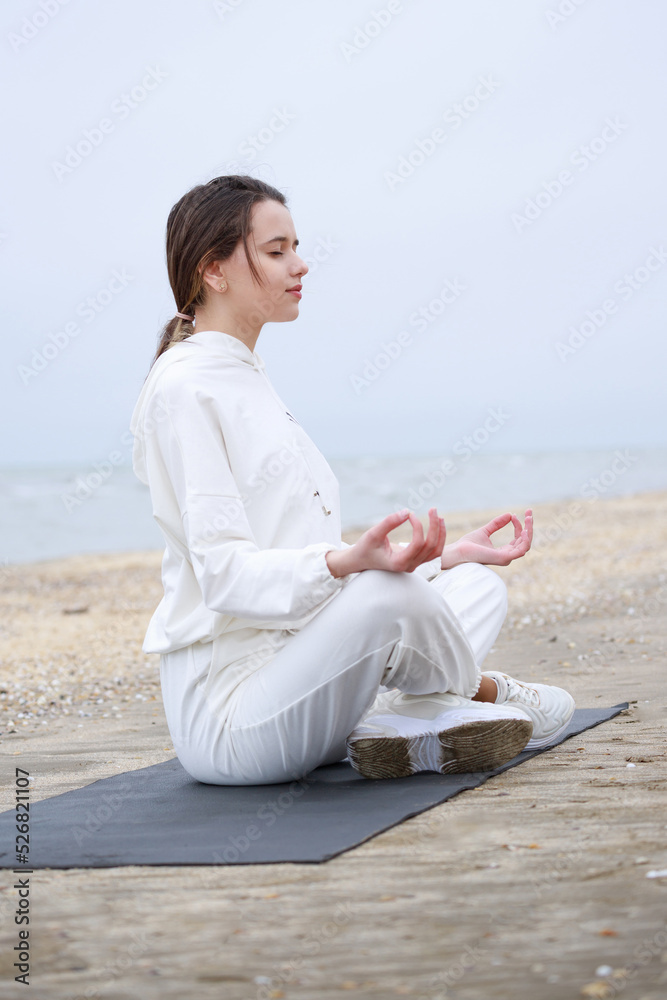 Adorable girl doing meditation on the beach