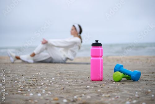 Pink water bottle and dumbbells on sand. Girl doing her exercises at beach