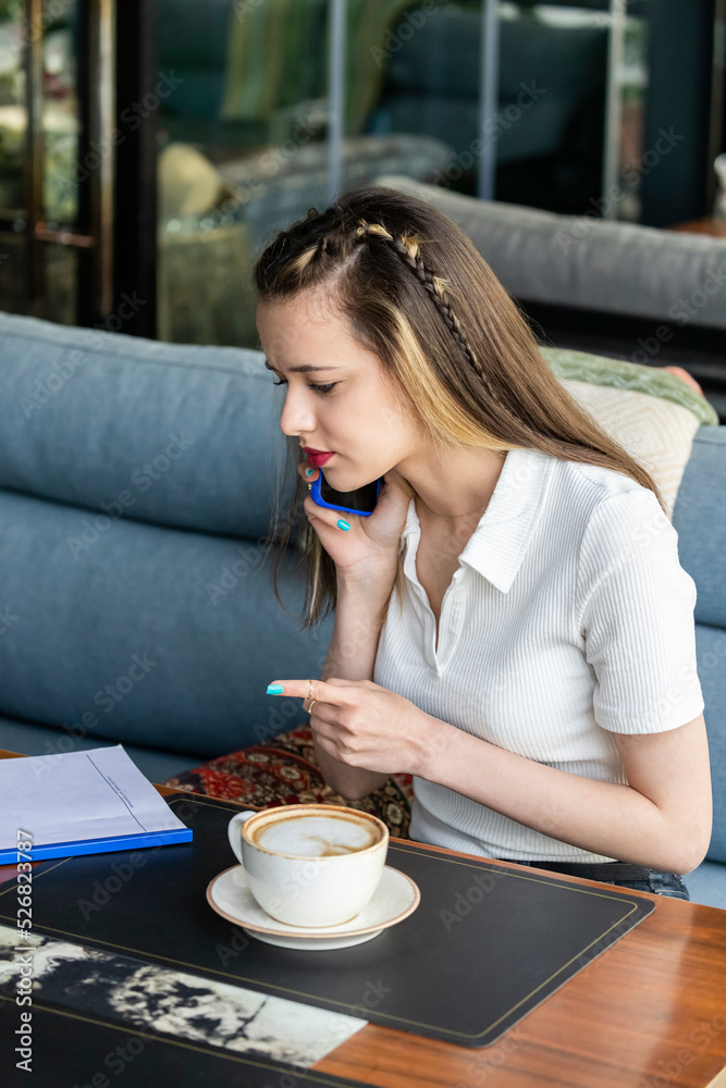 Cute young girl sitting at the restaurant on talking on the phone Cute young girl sitting at the restaurant on talking on the phone