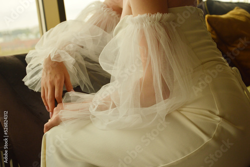 Bride's hands in a wedding dress. The bride sits leaning on the back of the chair.