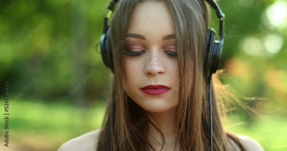 Millennial girl enjoying music, song, podcast, or audiobook in outdoor park. Woman holding cellphone with headphones Millennial girl enjoying music, song, podcast, or audiobook in outdoor park. Woman holding cellphone with headphones