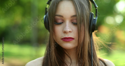 Millennial girl enjoying music, song, podcast, or audiobook in outdoor park. Woman holding cellphone with headphones