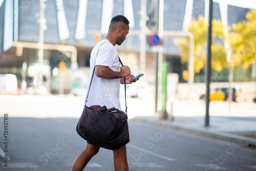 Man walking with sports bag and mobile phone on city street © mimagephotos