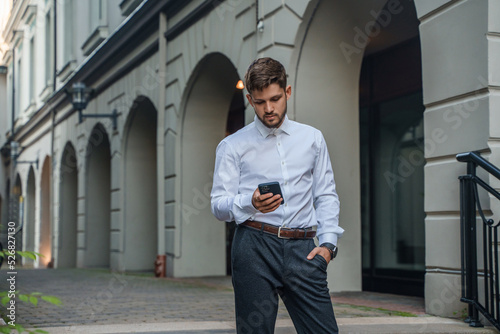 Shot of busy man dressed in formal clothes using his cellphone walking around city.