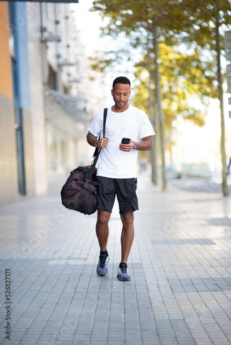 Man walking with sports bag and mobile phone on city street