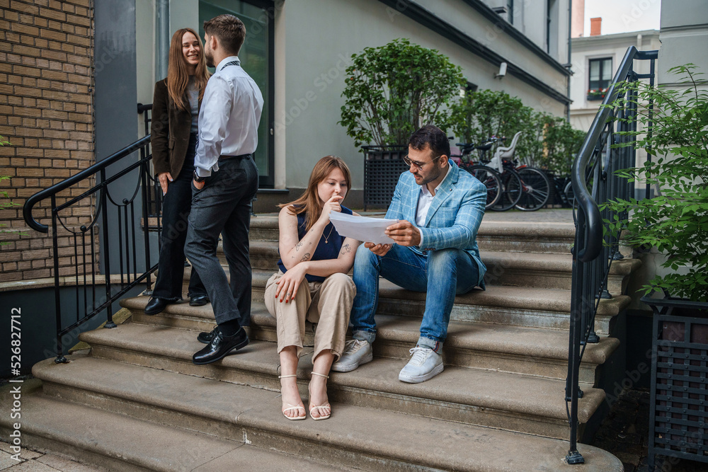 Fototapeta premium Portrait of four businesspeople analyzing documents and discussing their plans outdoors in city.