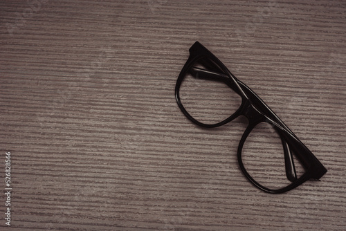 thick black rimmed reading glasses on desk at isolated wooden background. top view.