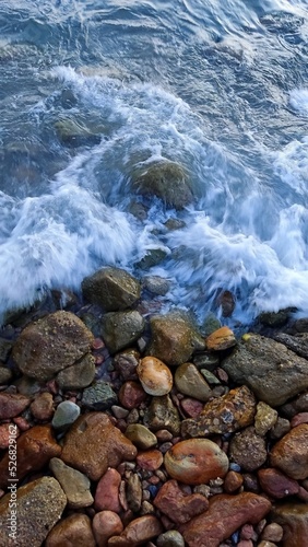Sea waves rolling on colorful coastal stones