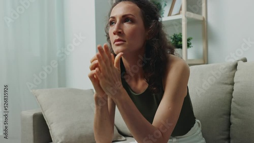 A woman sits on the couch at home and is nervous being stressed rubbing her hands