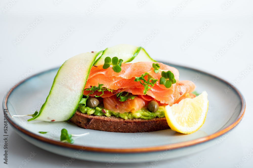 Toasted bread with mashed avocado, cucumber and smoked salmon on grey plate