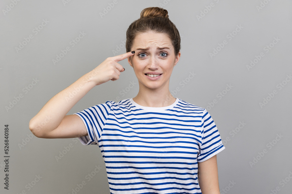 Crazy idea. Portrait of woman wearing striped T-shirt showing stupid gesture, looking with condemnation and blaming for insane plan, dumb suggestion. Indoor studio shot isolated on gray background. Crazy idea. Portrait of woman wearing striped T-shirt showing stupid gesture, looking with condemnation and blaming for insane plan, dumb suggestion. Indoor studio shot isolated on gray background.