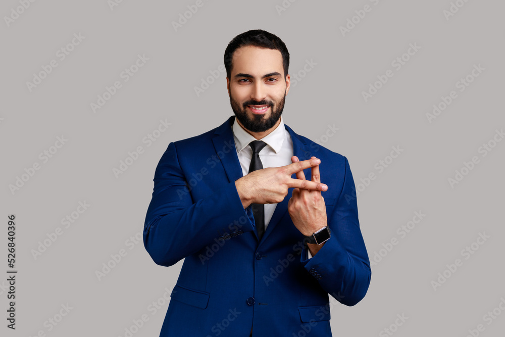 Positive optimistic bearded man crossing fingers to make hashtag sign and looking at camera with toothy smile, wearing official style suit. Indoor studio shot isolated on gray background. Positive optimistic bearded man crossing fingers to make hashtag sign and looking at camera with toothy smile, wearing official style suit. Indoor studio shot isolated on gray background.
