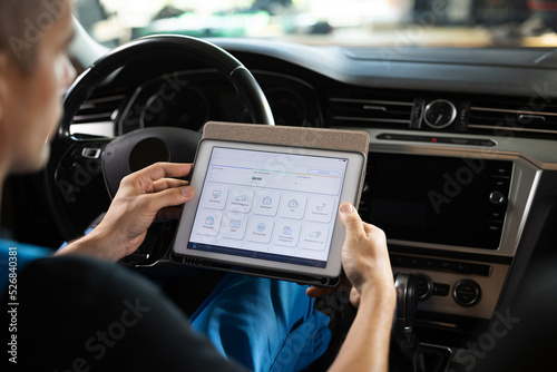 Automotive mechanic running diagnostics software on tablet. Unrecognizable vehicle service manager worker work in mechanics garage, check and maintenance to repair the engine car in workshop