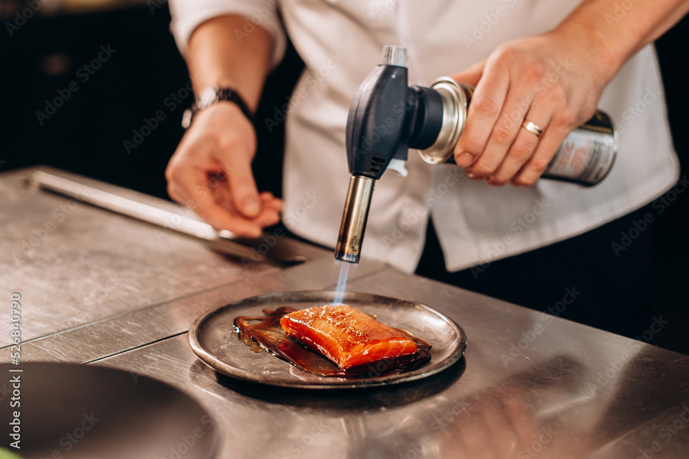 Chef fries salmon fish with a gas burner in a modern kitchen. The man prepares food at home. Cooking healthy and tasty food.