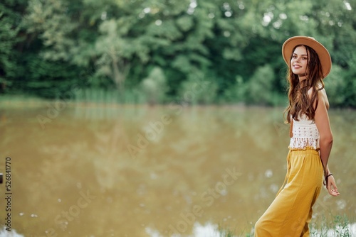 A young woman in a hippie look travels in nature by the lake wearing a hat and yellow pants in the fall