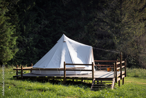 side view of glamping camping tent in green meadow surrounded by fir tree forest