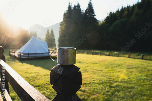closeup of metallic coffee cup in the morning with glamping camping ground in the background