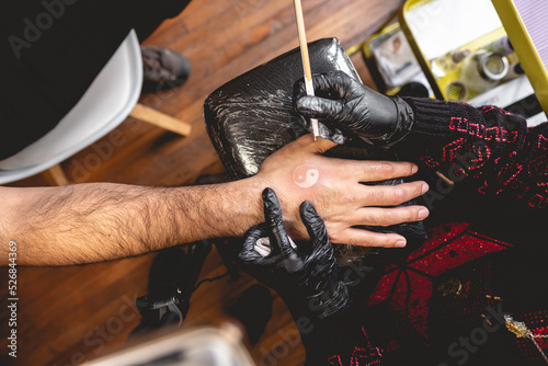 Obraz na plátně Detail of hands of tattoo artist with black gloves making a new tattoo with whit