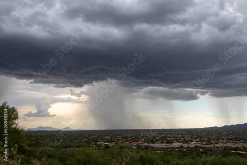 Monsoons in the Sonoran Desert with rain shafts or curtains coming down out of heavy dark gray clouds. Beautiful summer storm activity in the American Southwest. Pima County, Oro Valley, Arizona, USA.