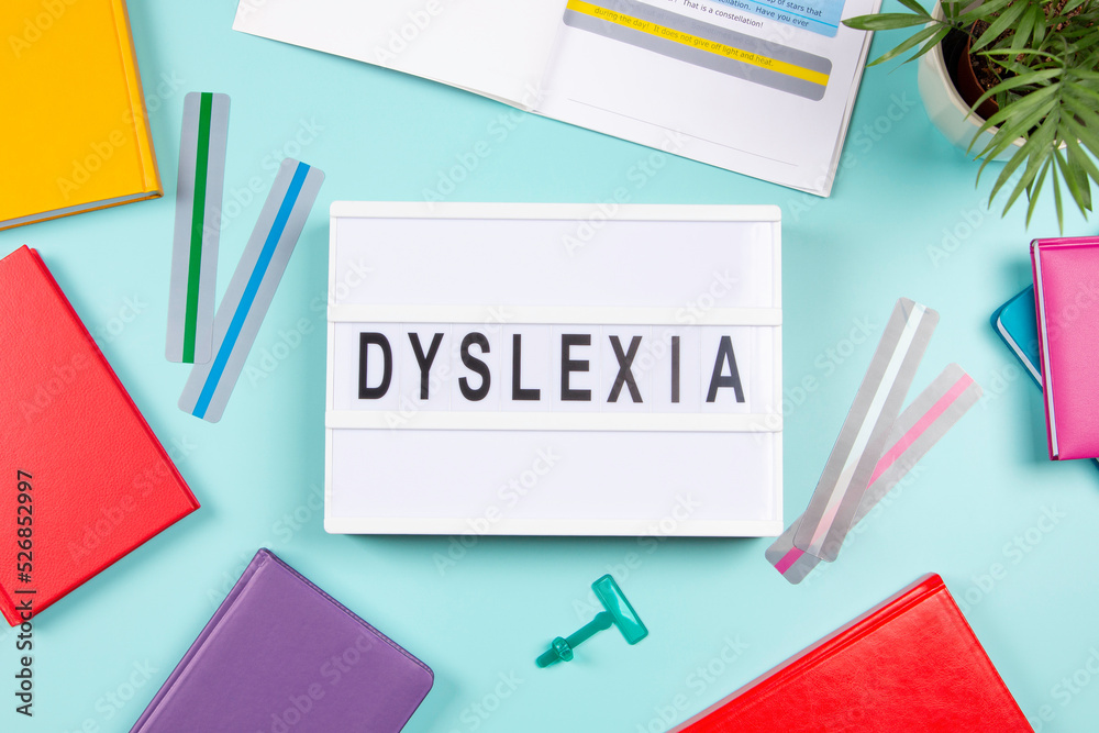 Dyslexia awareness, help children with reading, learning difficulties concept. Lightbox with DYSLEXIA word, colorful books and open book with reading highlight bookmark overlays strips. Top view Dyslexia awareness, help children with reading, learning difficulties concept. Lightbox with DYSLEXIA word, colorful books and open book with reading highlight bookmark overlays strips. Top view