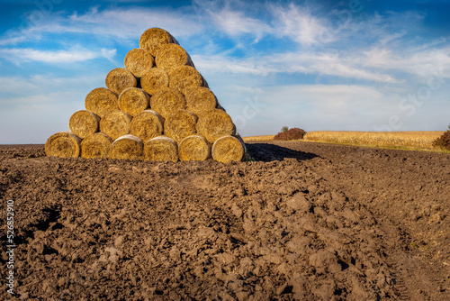 a pile of straw bales in the shape of a pyramid, stacked in a plowed field
