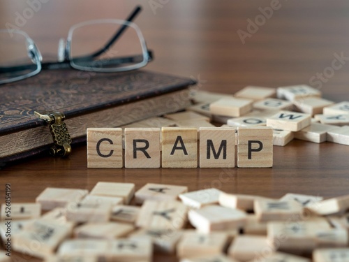 cramp word or concept represented by wooden letter tiles on a wooden table with glasses and a book