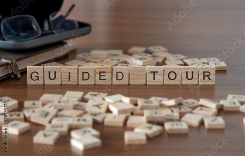 guided tour word or concept represented by wooden letter tiles on a wooden table with glasses and a book