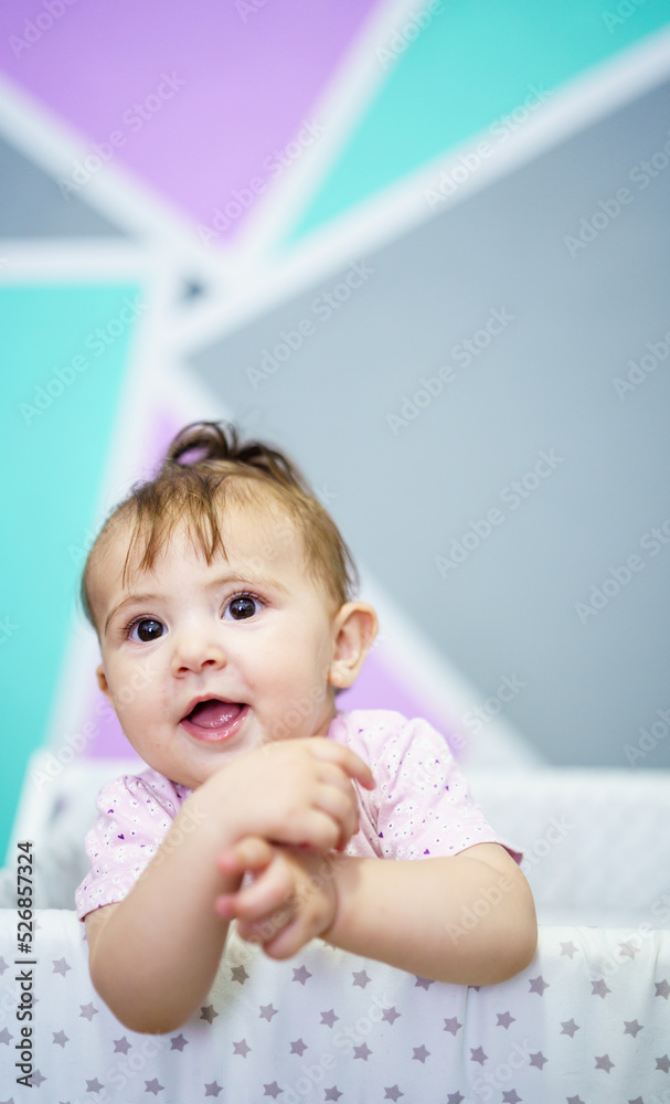 Cheerful baby standing in cradle and looking away Cheerful baby standing in cradle and looking away