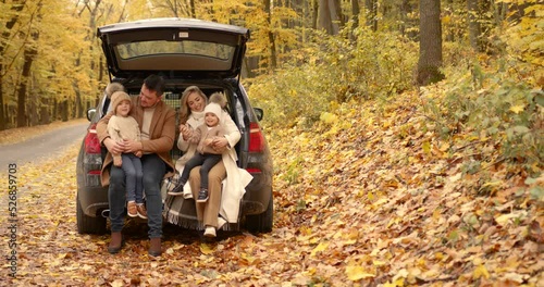 Happy family sitting in the trunk in the autumn park