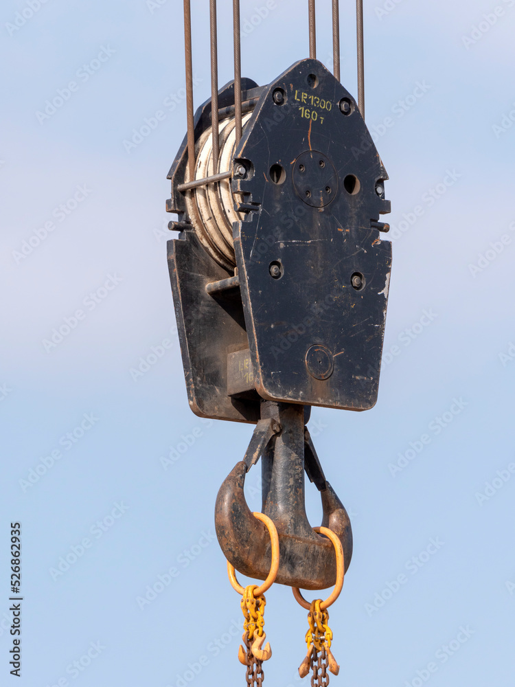 Crane hook with red and white stripes hanging, blue sky in background Crane hook with red and white stripes hanging, blue sky in background