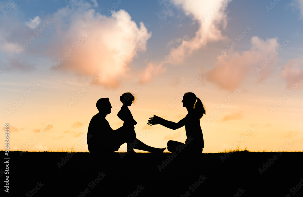 Happy family moment in nature. Mother, father and child sitting together on park grass together at sunset.