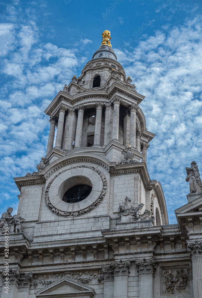 London, England, UK - July 6, 2022: St. Paul's Cathedral. Closeup of NW tower spire with golden top and no clock. Stone statues on corners and above under blue cloudscape.