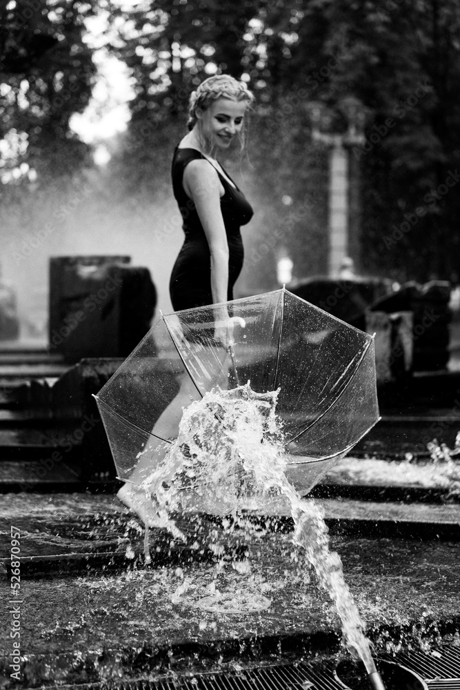 Obraz premium Happy woman having fun at the city fountain on a summer day with a transparent umbrella.