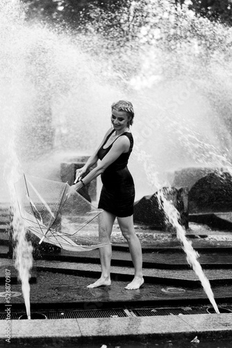 Happy woman having fun at the city fountain on a summer day with a transparent umbrella. © Yuliya Kirayonak