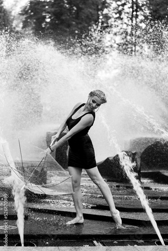Happy woman having fun at the city fountain on a summer day with a transparent umbrella. © Yuliya Kirayonak