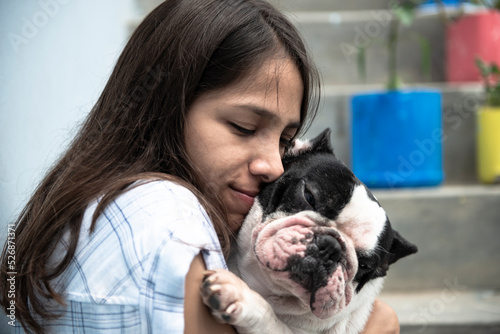 Young latin woman caresses and hugs her dog (french bulldog) next to the stairs © BlkG