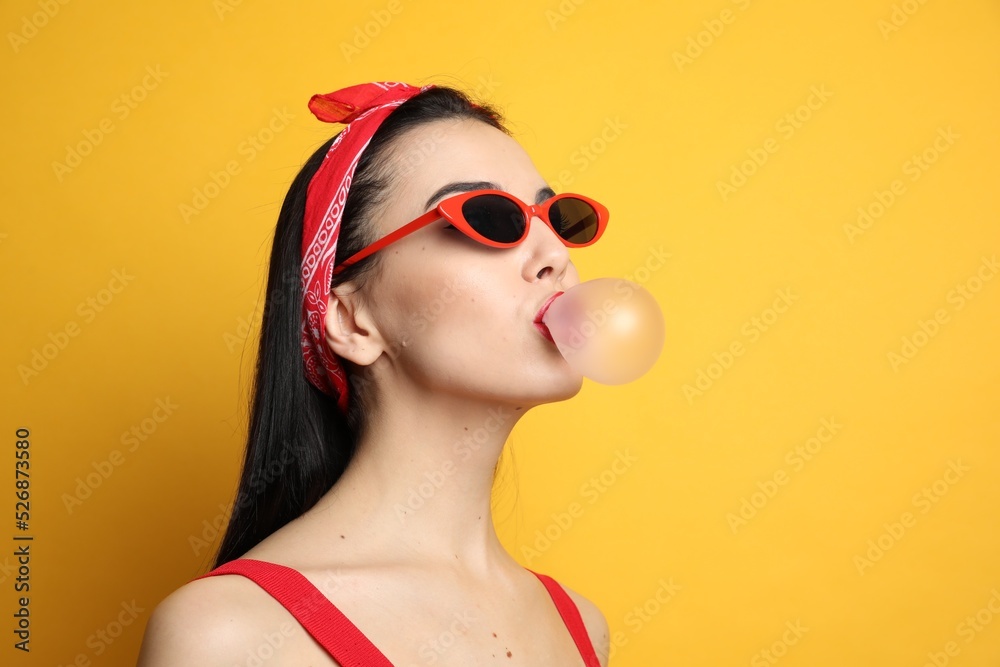 Fashionable young woman in pin up outfit blowing bubblegum on yellow background, space for text Fashionable young woman in pin up outfit blowing bubblegum on yellow background, space for text