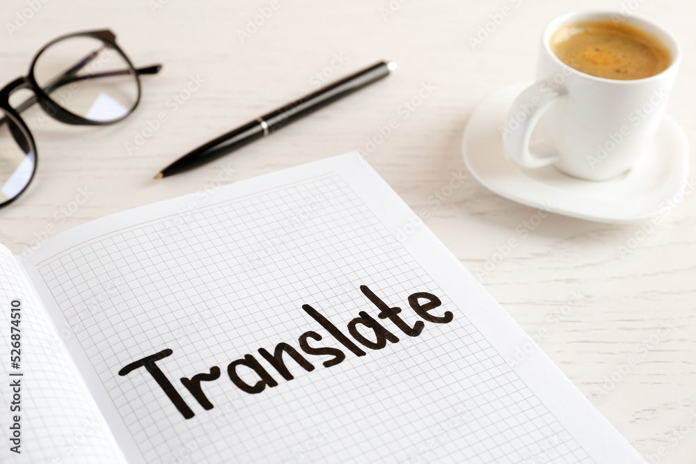 Notebook with written word Translate, pen, eyeglasses and cup of coffee on white wooden table Notebook with written word Translate, pen, eyeglasses and cup of coffee on white wooden table