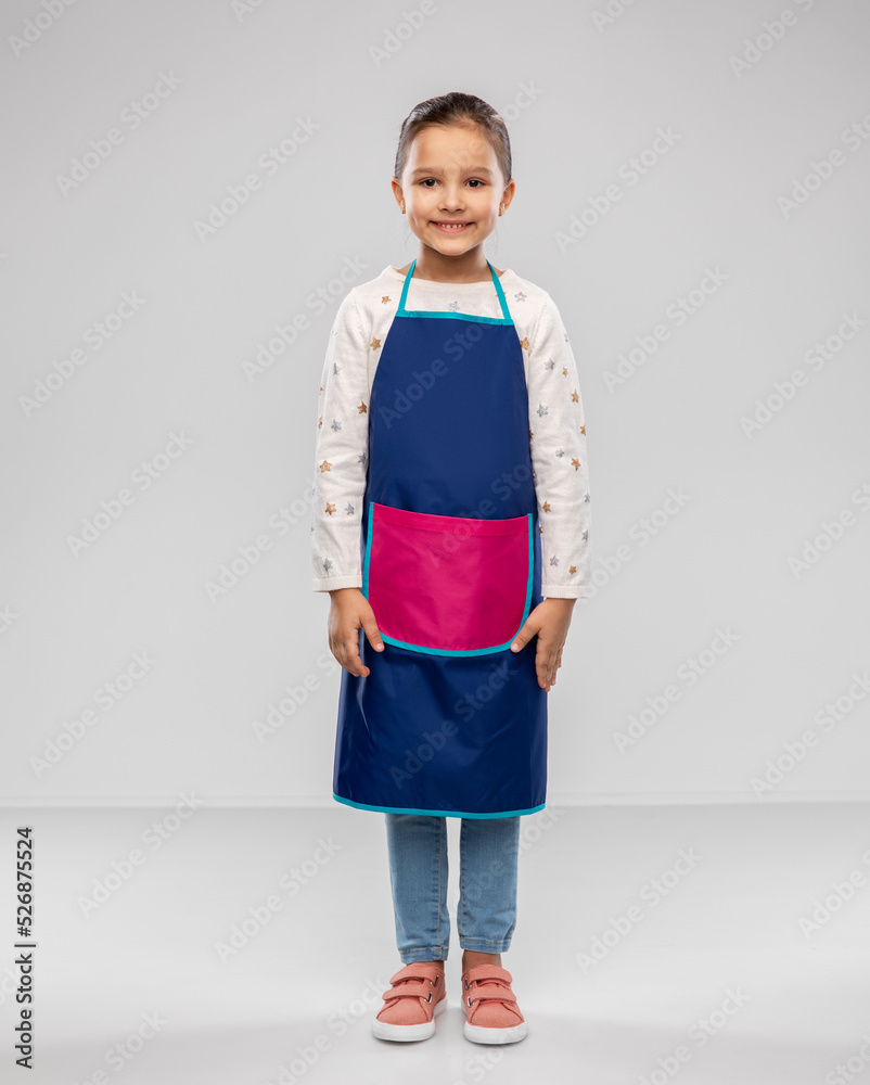 Fototapeta premium cooking, culinary and profession concept - happy smiling little girl in kitchen apron over grey background