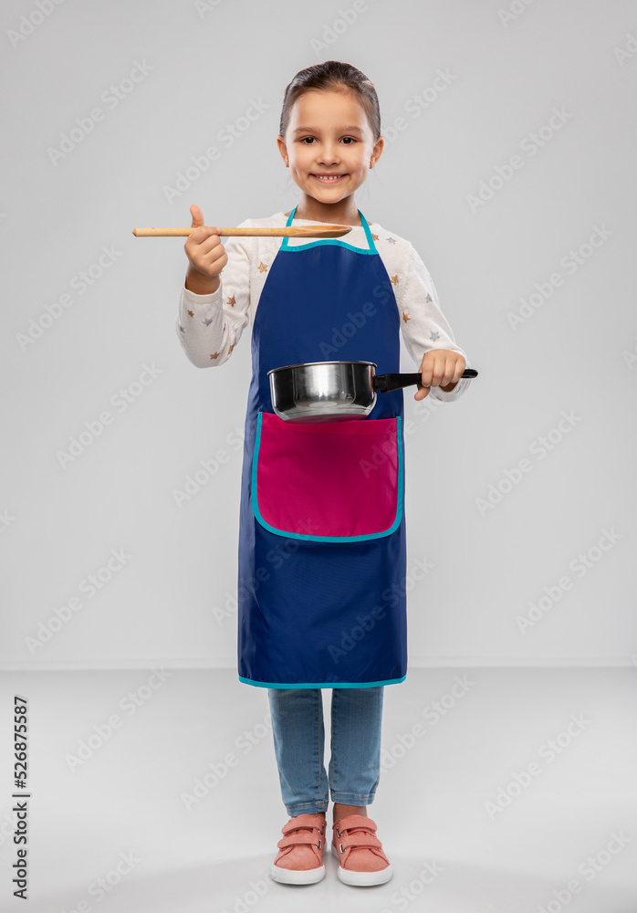 culinary and profession concept - happy smiling little girl in apron with saucepan and wooden spoon cooking food over grey background culinary and profession concept - happy smiling little girl in apron with saucepan and wooden spoon cooking food over grey background