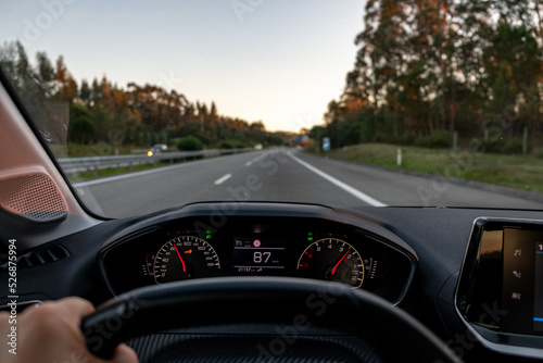 Driver view to the speedometer at 87 kmh or 87 mph and the road blurred in motion, night fall view from inside a car of driver POV of the road landscape.