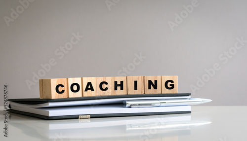 Coaching word on wood block cubes, on top of notepad and pen.