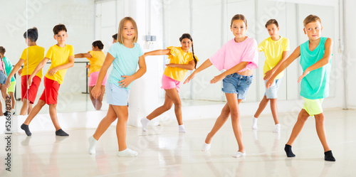 Smiling preteen girls and boys training movements of modern energetic dancing in children studio. © JackF