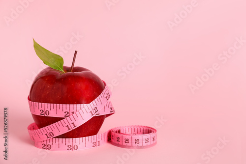 Fresh red apple with measuring tape on pink background. Space for text