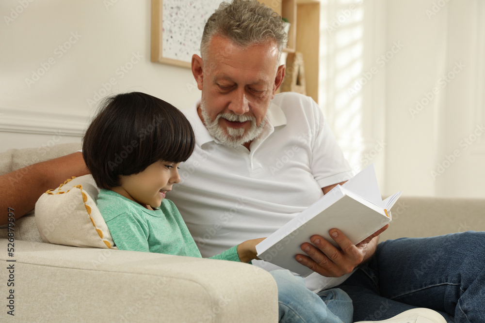 Obraz premium Happy grandfather with his grandson reading book together at home