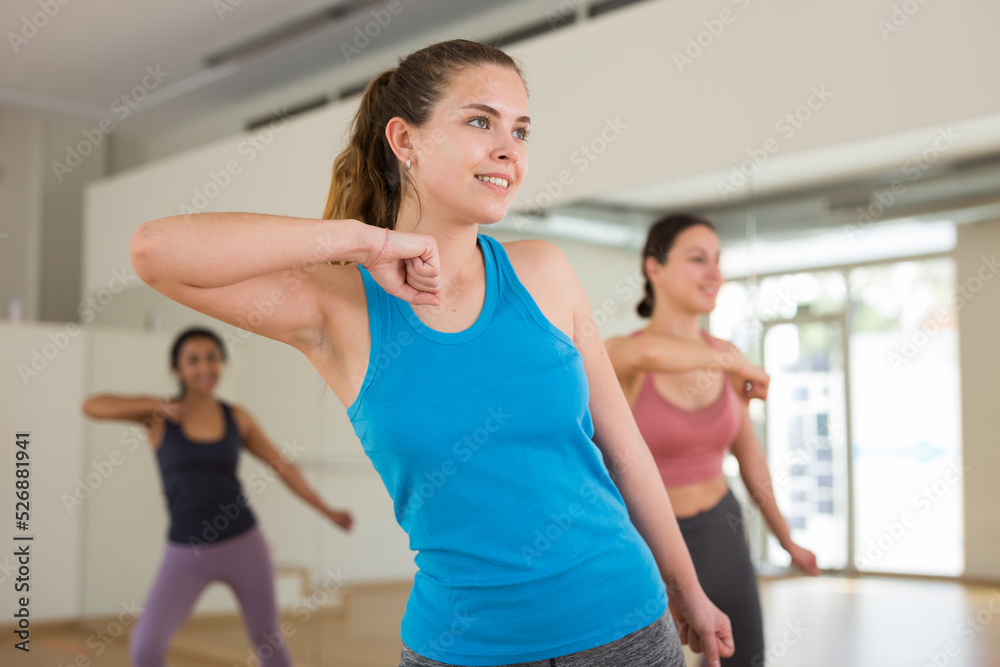 Positive young woman enjoying active dances in female group in modern dance studio.