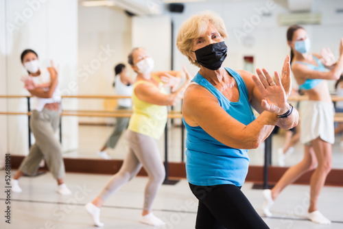Old lady dancing with other women in face masks during group training in studio.