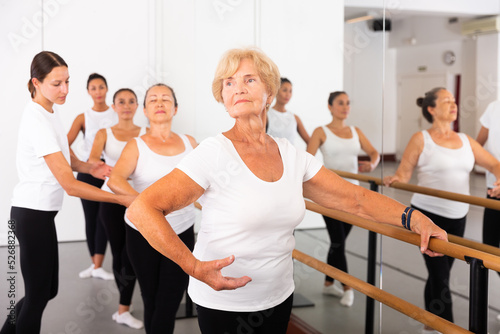 Various aged women exercising ballet dance moves. Woman trainer correcting her students.