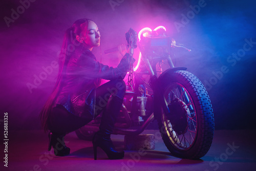 Beautiful asian girl a motorbiker with a chain in hand near the old motorcycle in the neon lights concept.