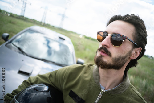 Rally car driver in the sunglasses stands on the countryside road concept.
